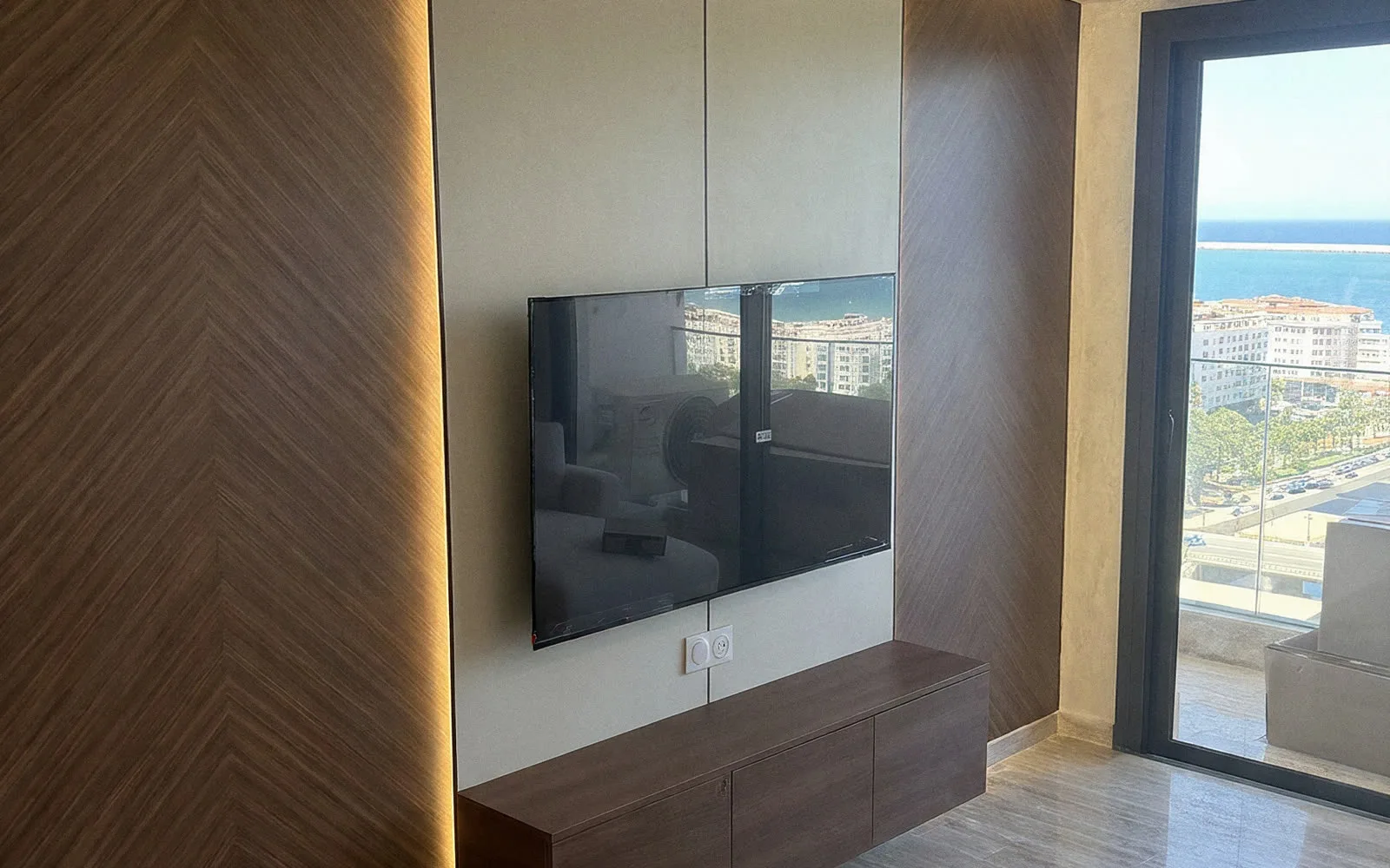 Mur TV en panneaux chevron noyer avec LED dans un appartement de location courte durée avec vue mer à Tanger