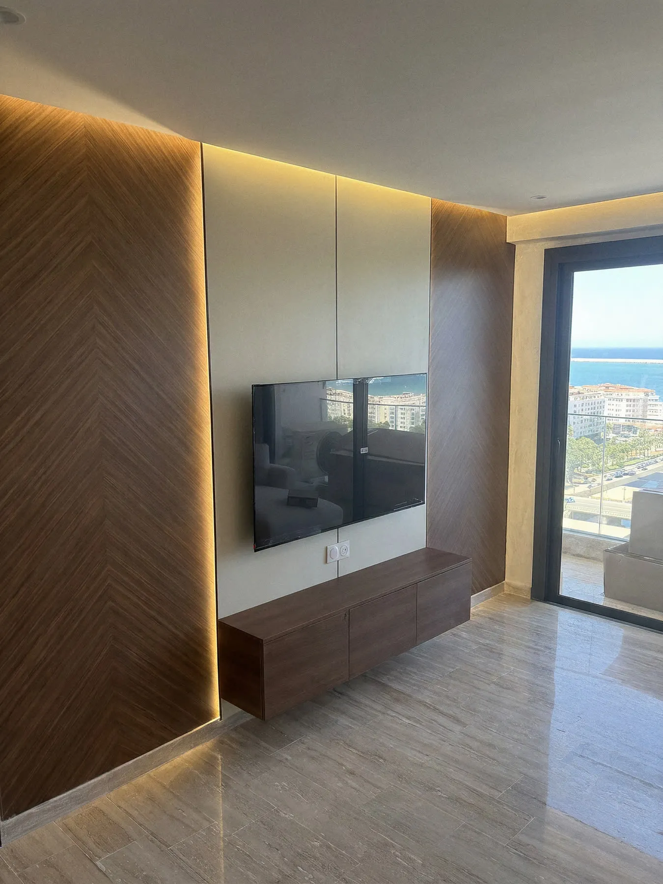 Après : mur TV en panneaux chevron noyer et LED avec meuble suspendu, appartement vue mer à Tanger