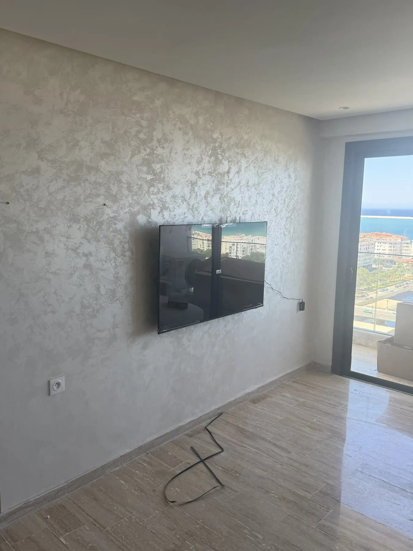 Avant : salon d'appartement locatif avec mur nu et TV, avant habillage mural
